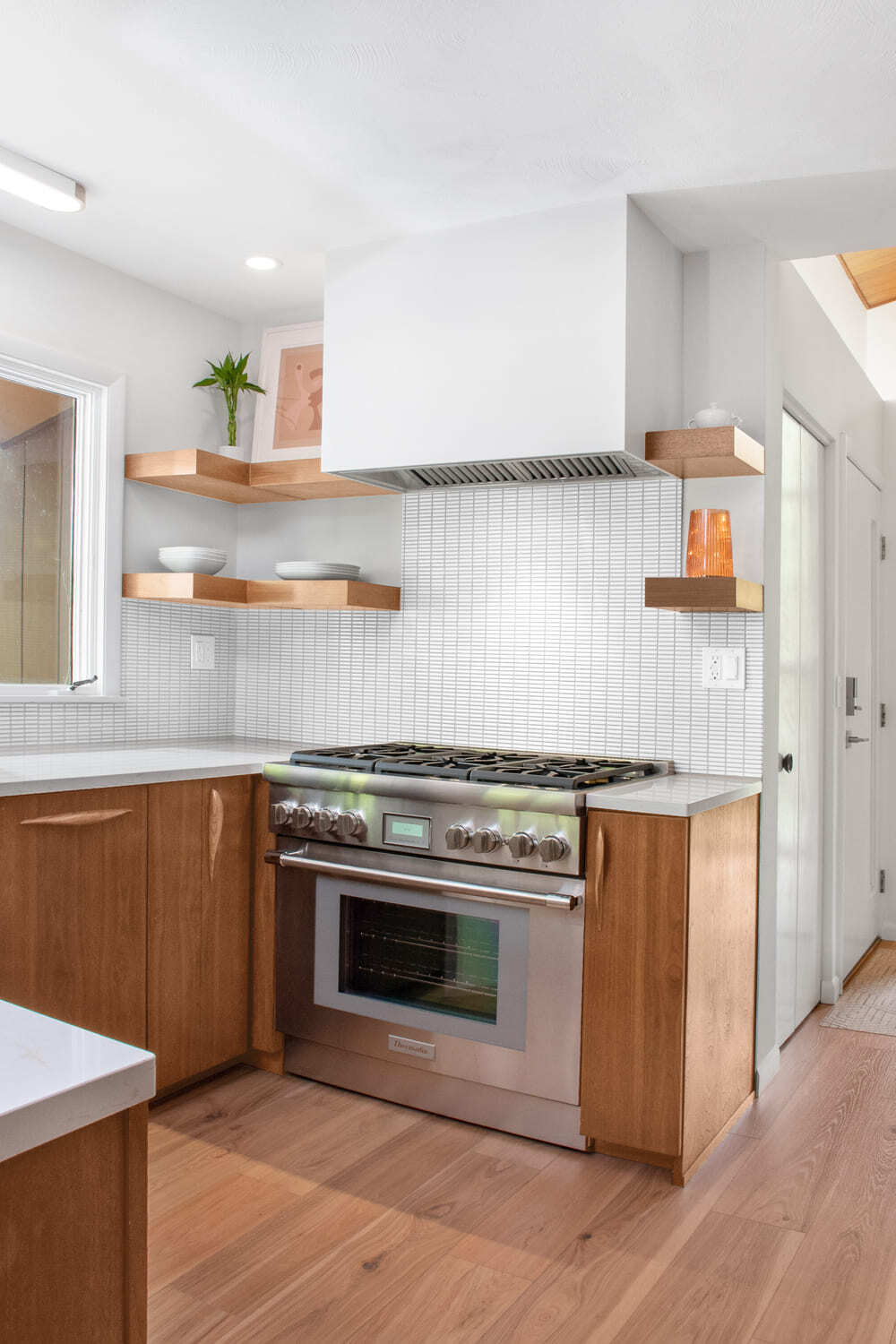 Range set in custom cabinets with floating shelves and range hood above in Lafayette kitchen remodel